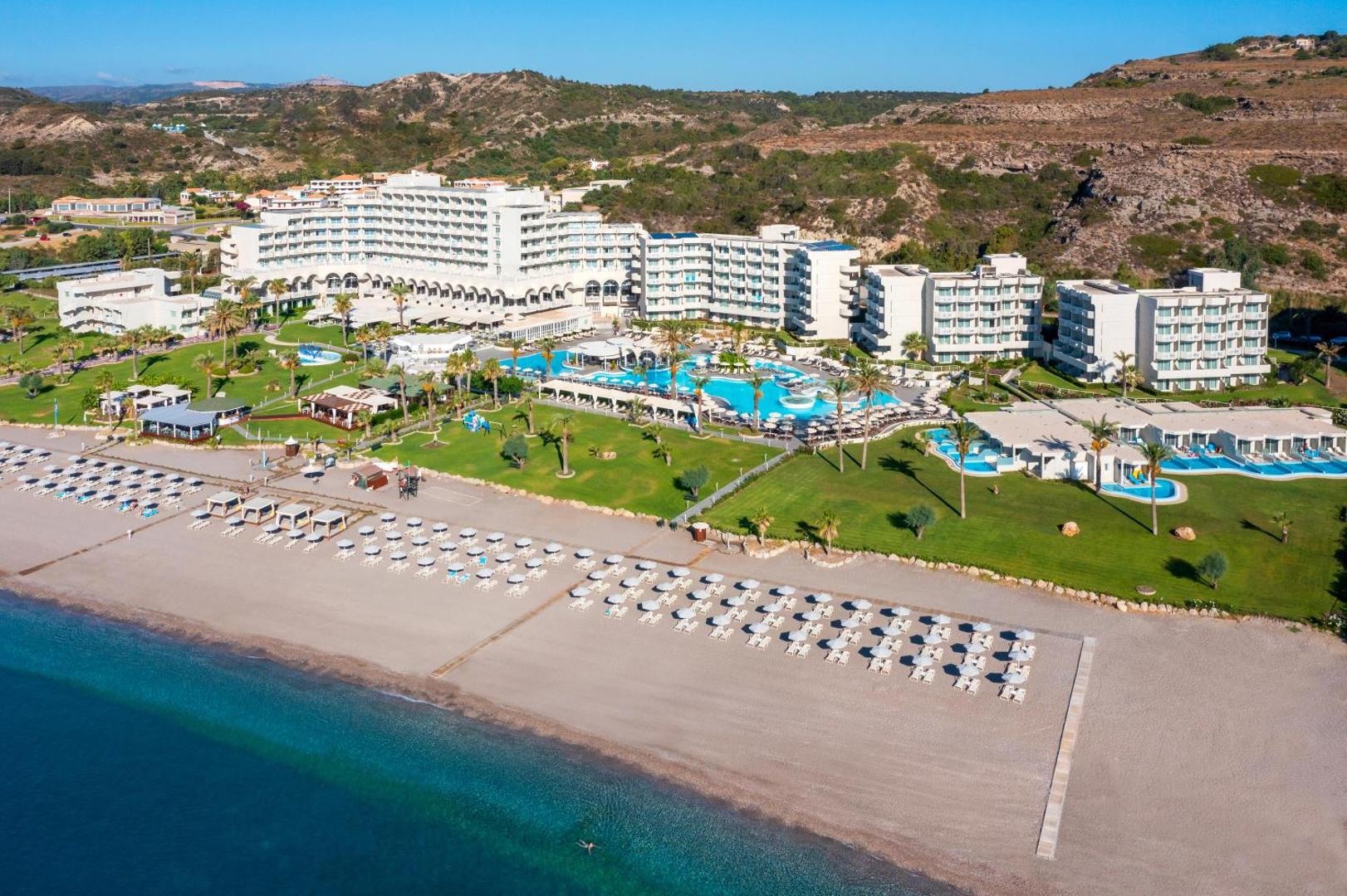 Rodos Palladium Leisure & Wellness panorāmas skats no putna lidojuma Rodas salā — viesnīcas korpusi, baseini un plaša smilšu pludmale pie Egejas jūras