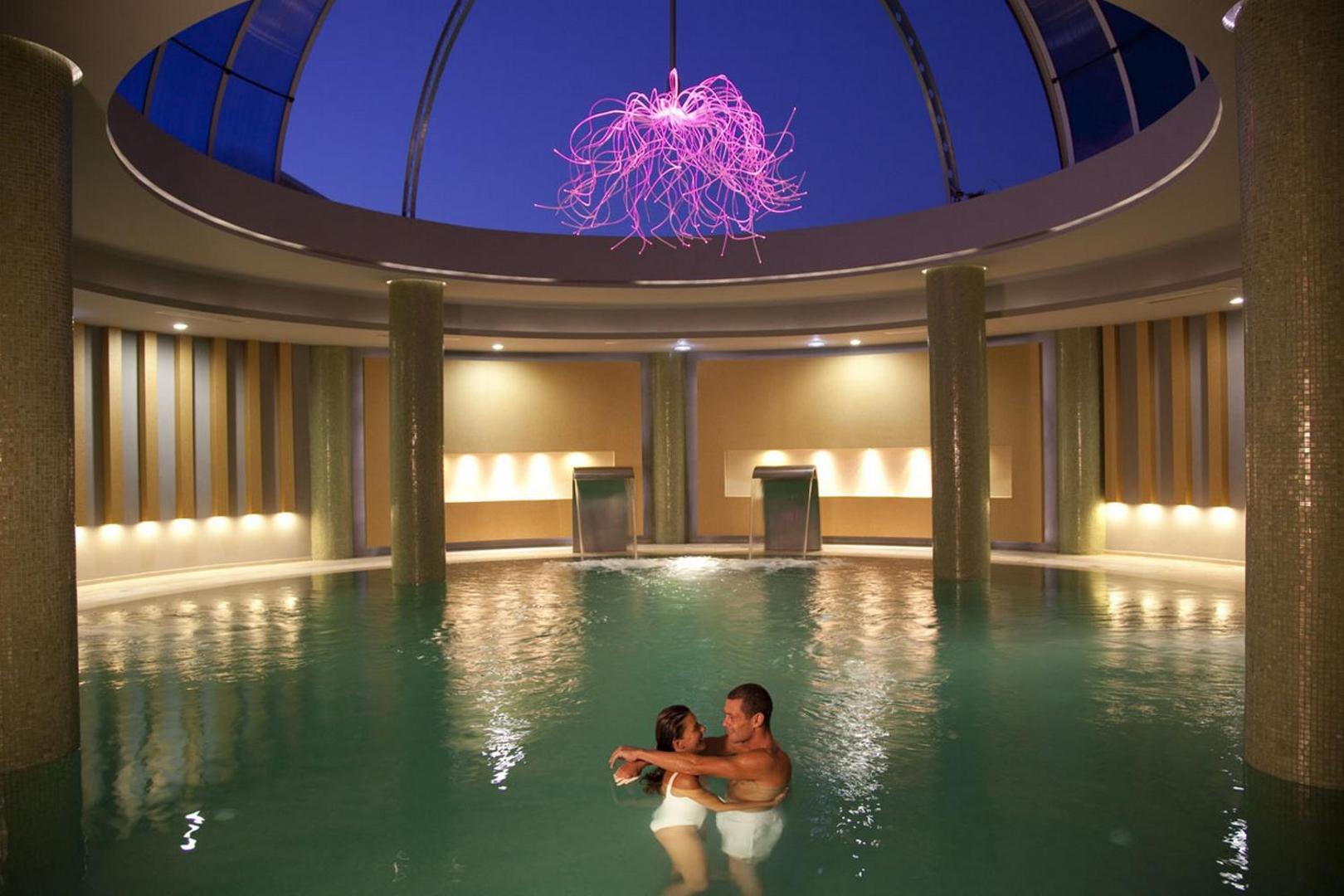 Sentido Port Royal Villas & Spa iekštelpu spa baseins ar kupolu un dekoratīvu apgaismojumu Rodā — pāris bauda atpūtu siltā ūdenī