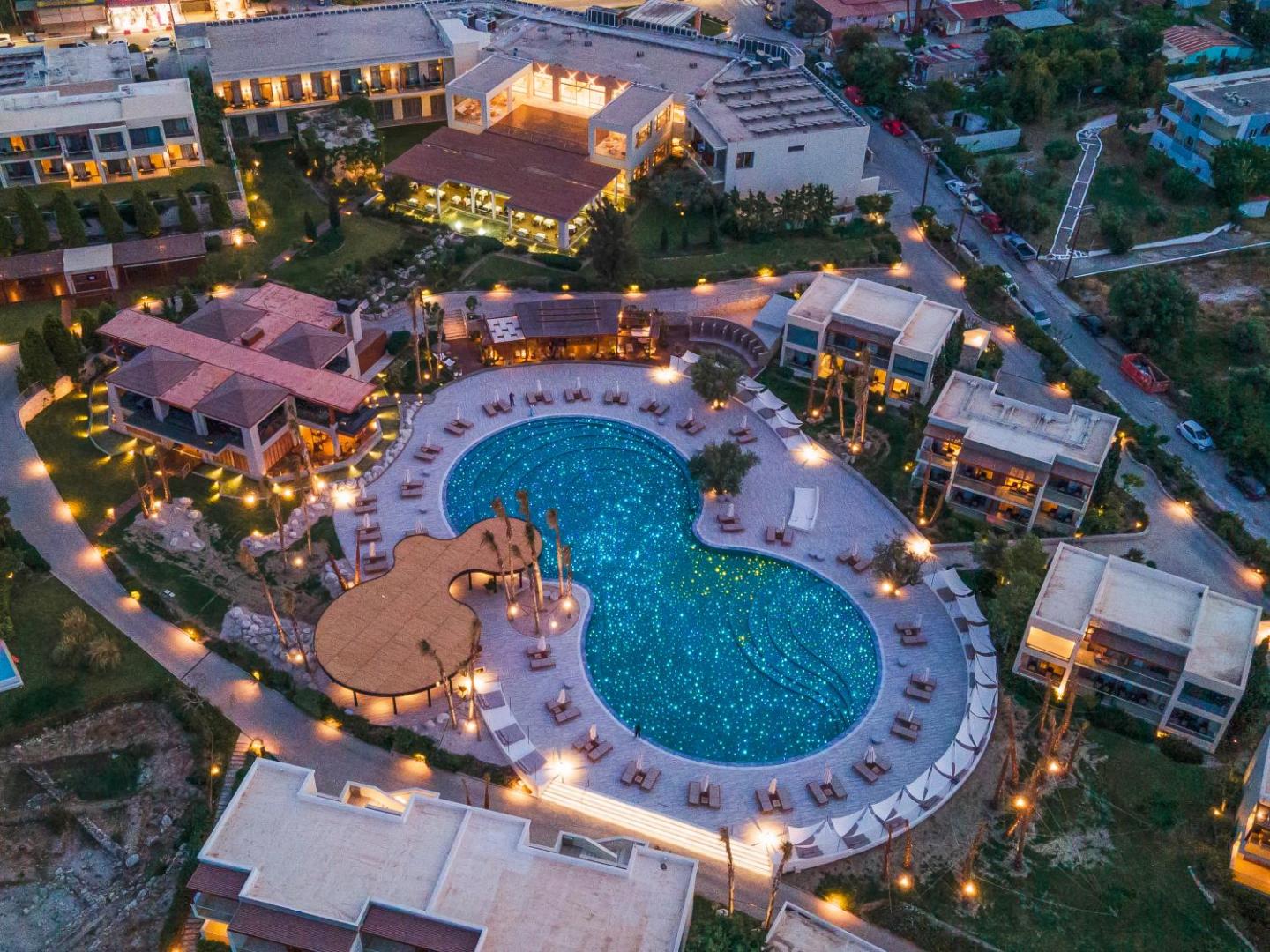 Sentido Port Royal Villas & Spa teritorijas skats no augšas vakarā ar izgaismotu baseinu un viesnīcas korpusiem