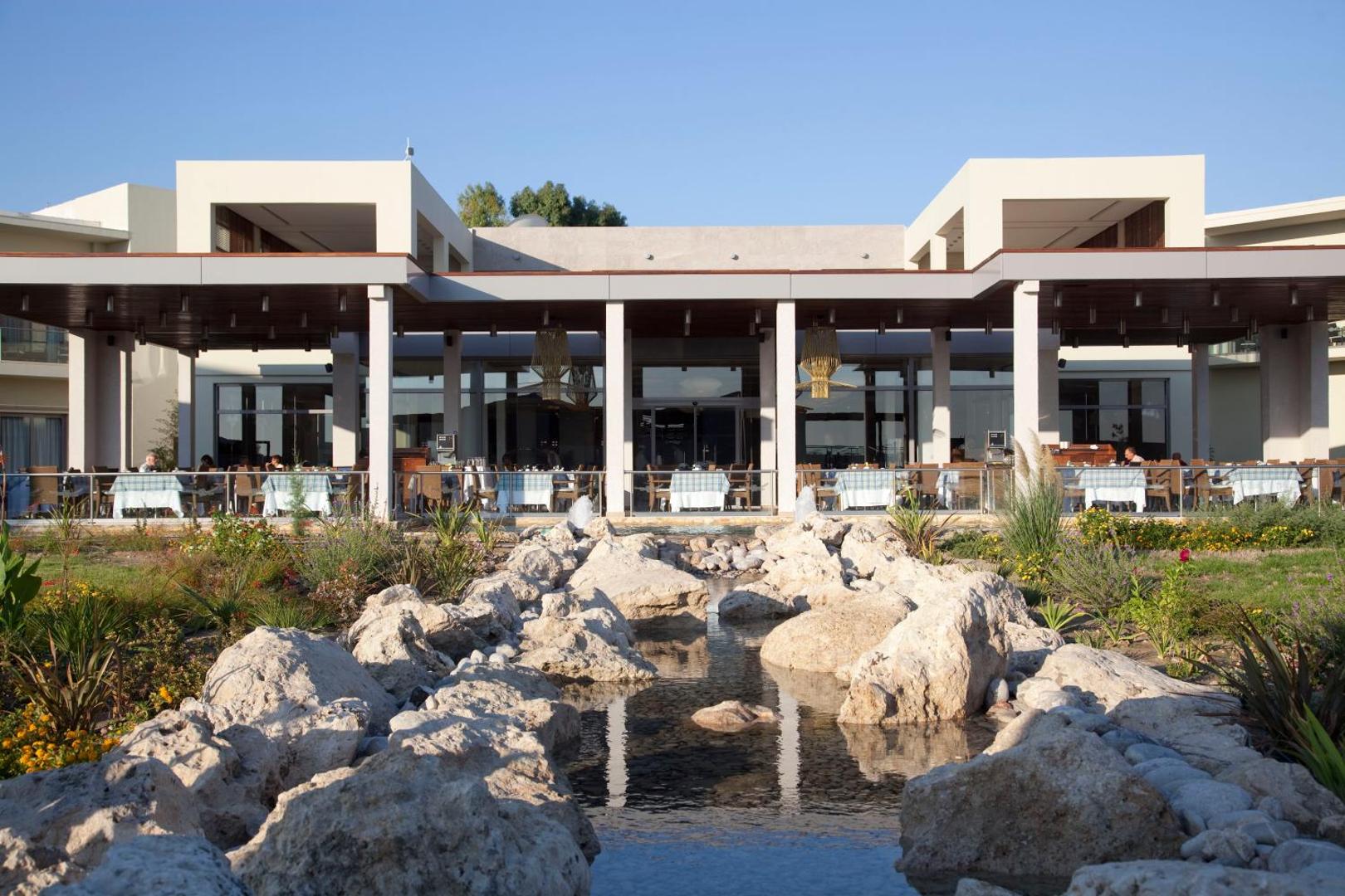 Sentido Port Royal Villas & Spa viesnīcas galvenā ēka un restorāns ar dekoratīvu akmens dīķi priekšplānā