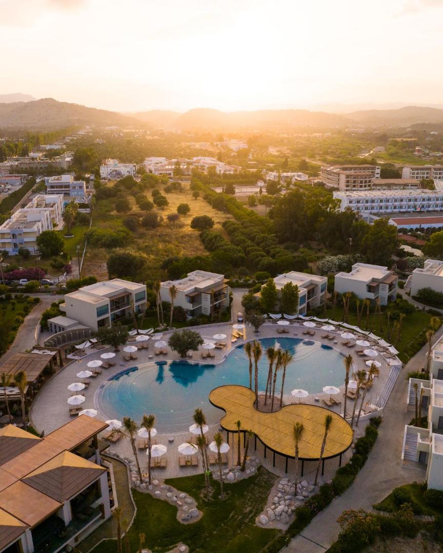 Sentido Port Royal Villas & Spa skats no augšas uz galveno baseinu un bungalo saulrietā Kolimbijā, Rodas salā