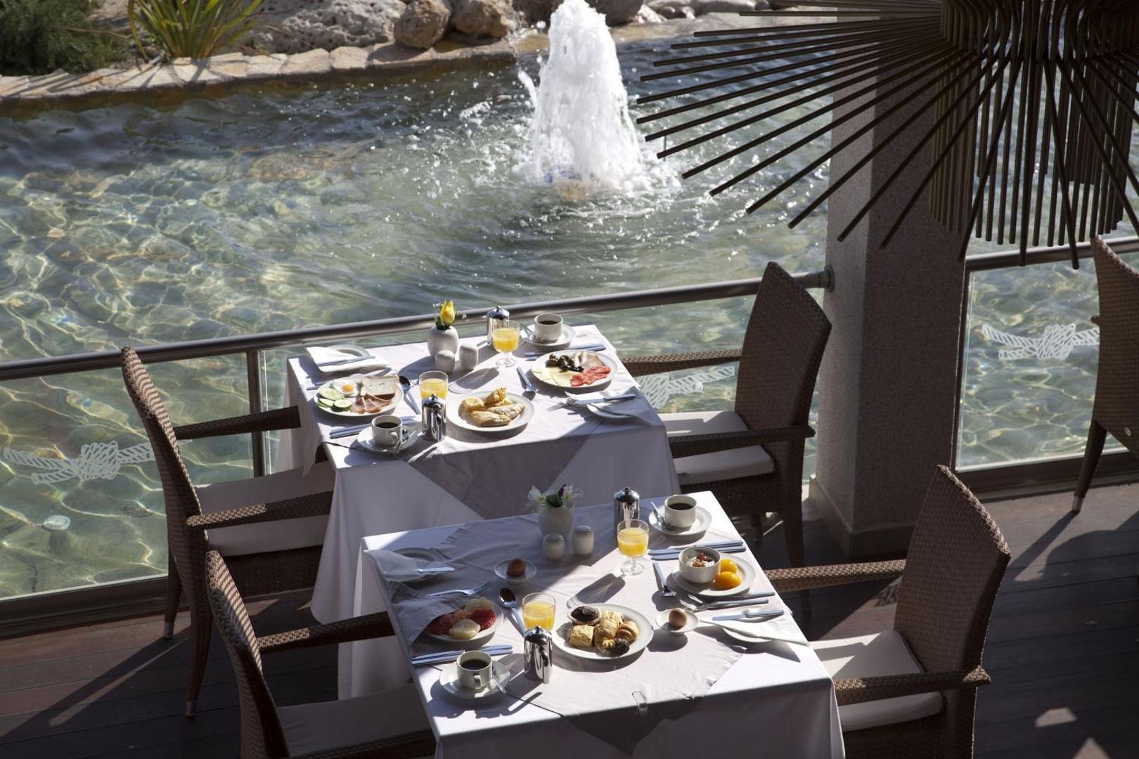 Sentido Port Royal Villas & Spa restorāna terase ar klātiem brokastu galdiem pie dekoratīva ūdens baseina ar strūklaku Rodas salā.