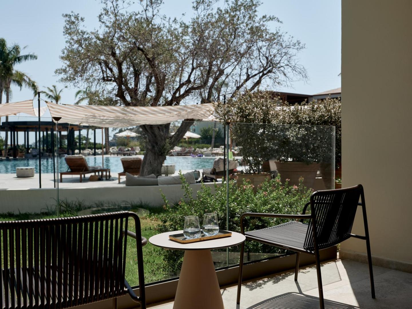 Sentido Port Royal Villas & Spa terase ar krēsliem un skatu uz āra baseinu, olīvkokiem un atpūtas zonu Rodā
