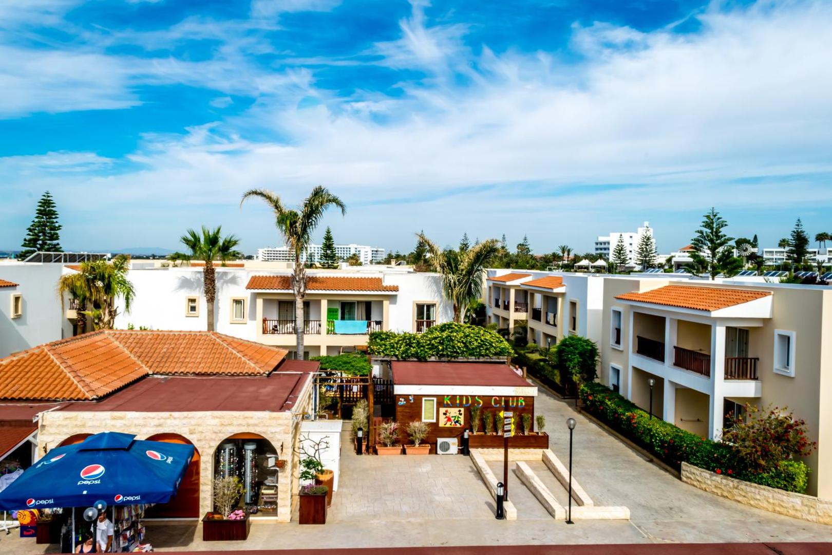 Aktea Beach Village iekšpagalms ar bērnu klubu Kids Club, palmām un zemu apbūvi — droša un sakopta vide ģimenes atpūtai