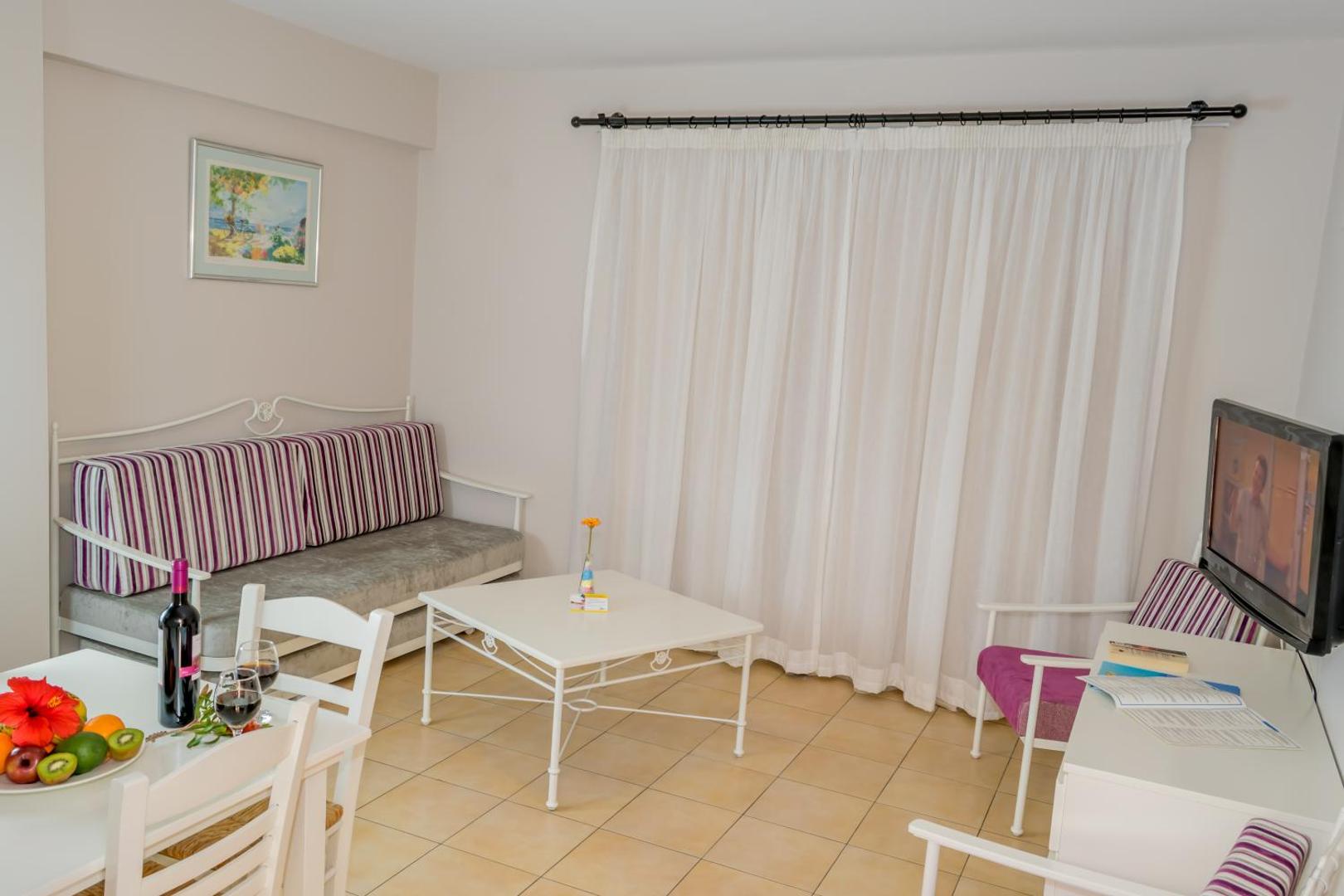 Aktea Beach Village numura interjers ar atpūtas krēsliem, galdiņu un vīna glāzēm — mājīga atmosfēra Kipras kūrortā