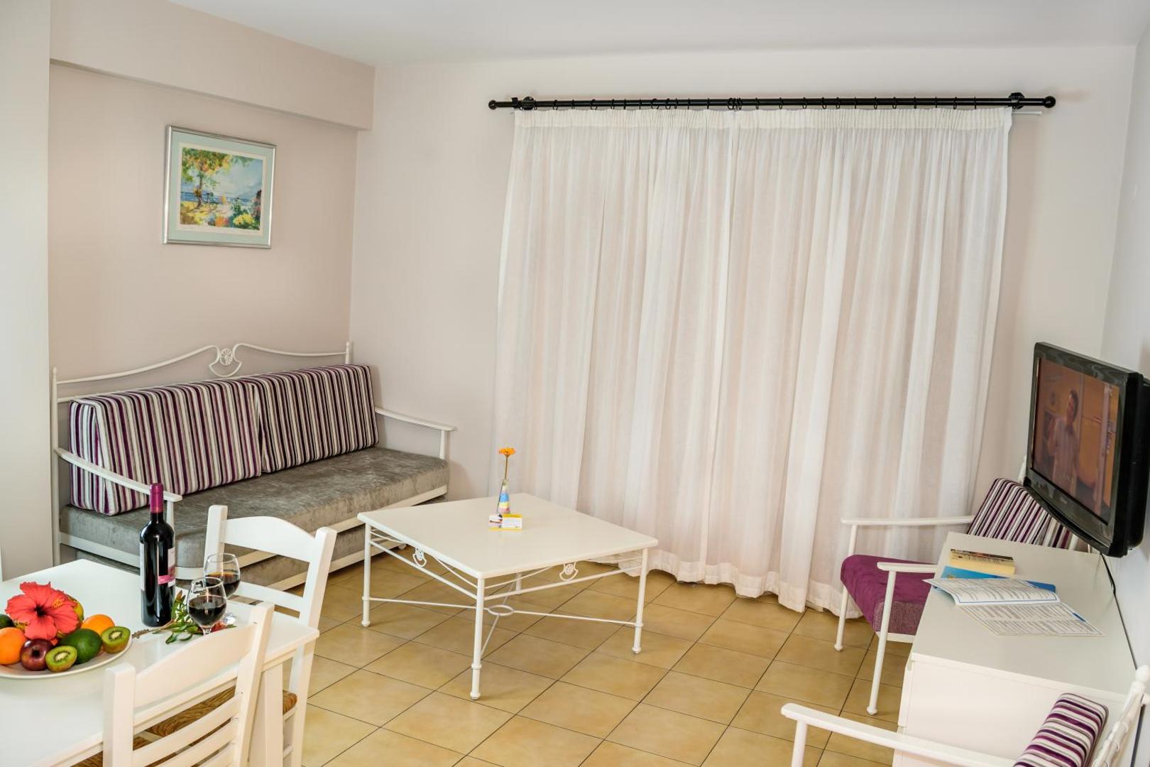 Aktea Beach Village viesistabas zona ar dīvānu, televizoru un augļu plati uz galda — plašs numurs ģimenes atpūtai