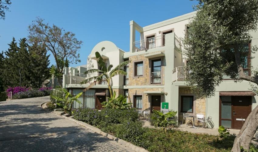Duja Bodrum ciemata stila numuri ar akmens apdari un balkoniem, ko ieskauj olīvkoki un tropiskie augi dārza teritorijā