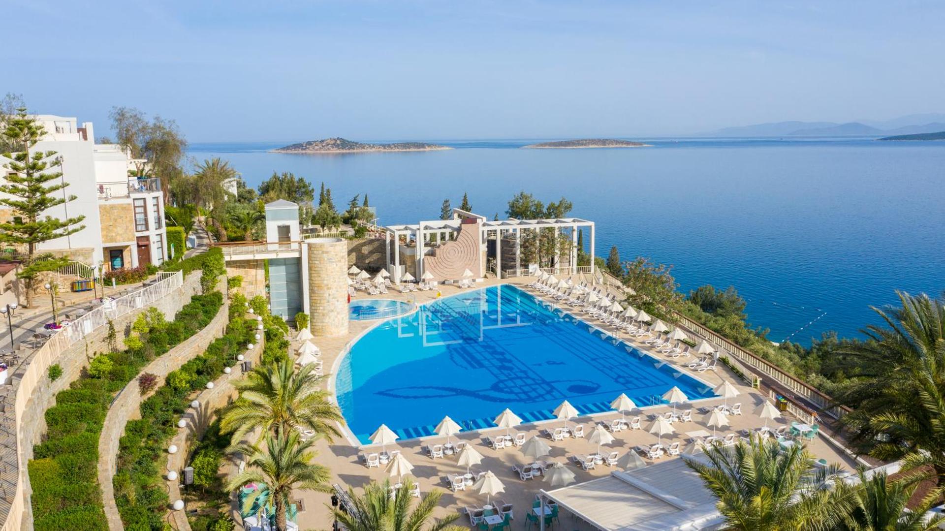 Duja Bodrum galvenais āra baseins ar skatu uz Egejas jūru un salām — plaša atpūtas zona ar saulessargiem un palmām