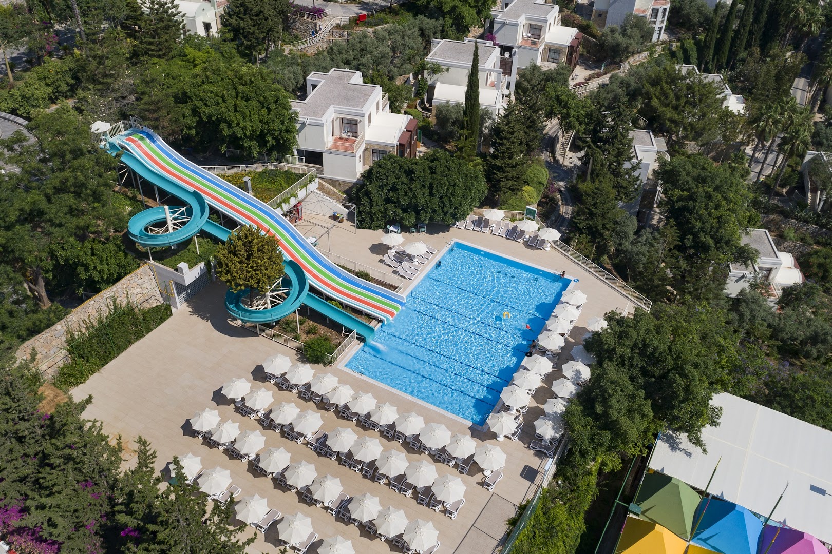 Duja Bodrum akvaparks no putna lidojuma — krāsaini ūdens slidkalniņi, baseins un sauļošanās zona zaļumu ieskāvumā