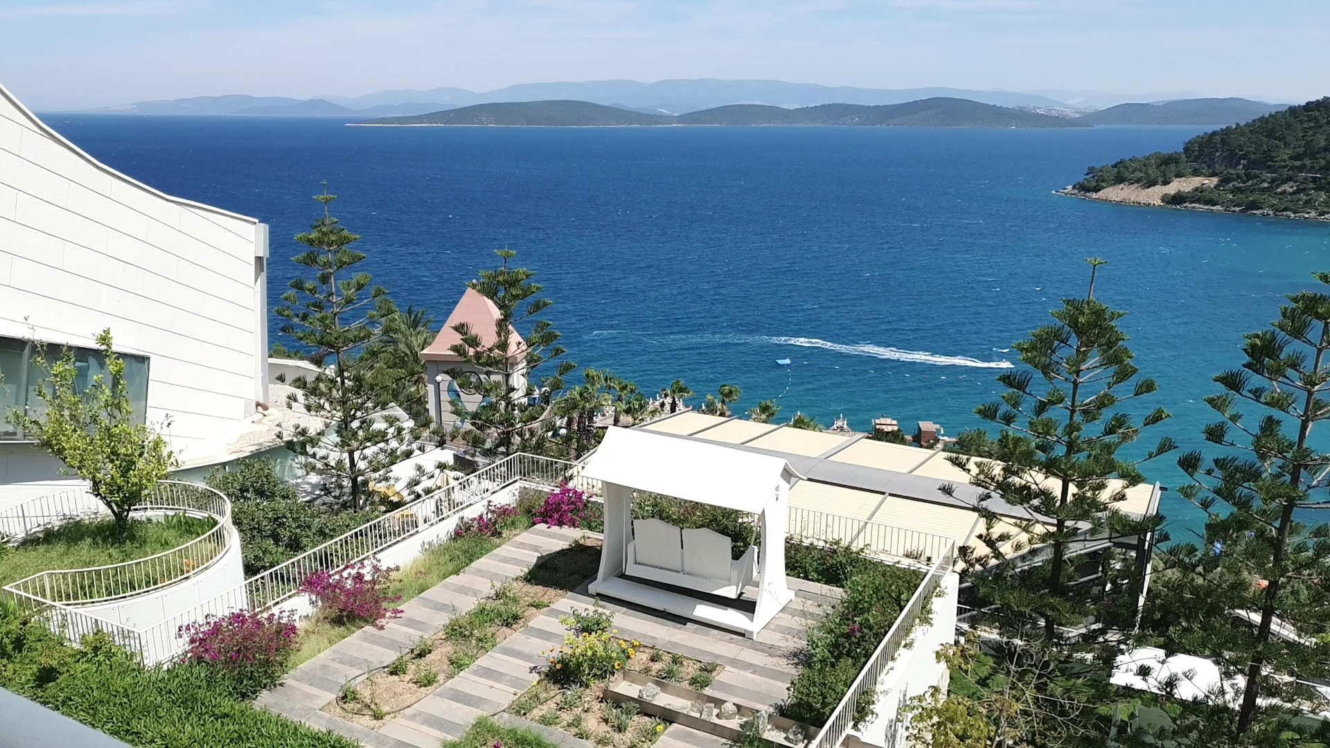 Duja Bodrum viesnīcas terase ar baltām šūpolēm un skatu uz Egejas jūras piekrasti, apkārtnē zaļojoši dārzi un kalni