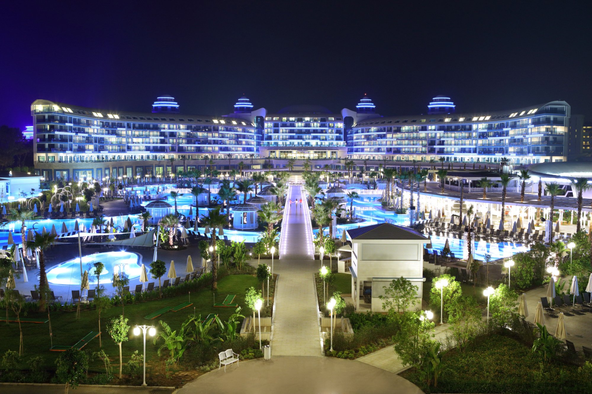 Sueno Hotels Deluxe Belek nakts skats uz galveno ēku, baseiniem un izgaismotiem gājēju celiņiem dārzā