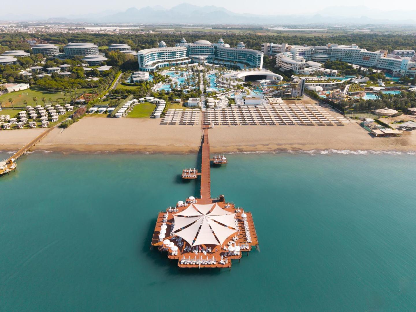 Sueno Hotels Deluxe Belek aerofoto ar plašu koka piestātni un atpūtas zonu jūrā pie Belekas pludmales