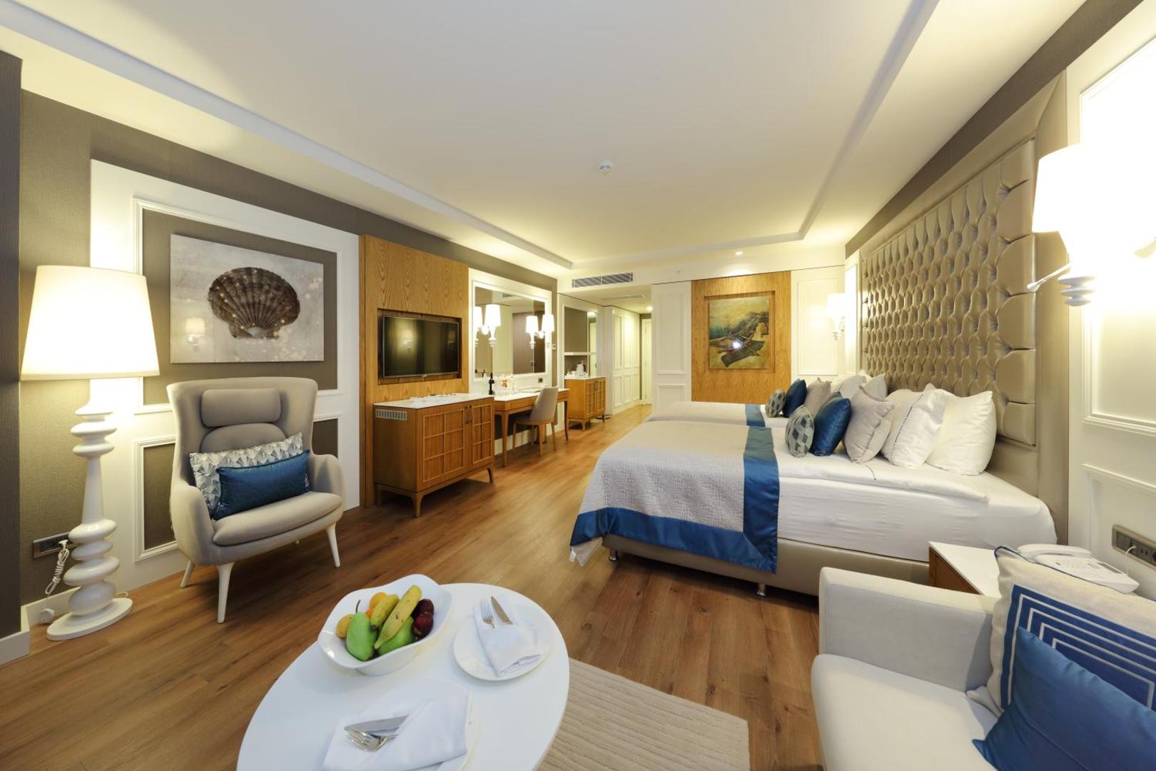 Sueno Hotels Deluxe Belek moderns numurs ar divām gultām, atpūtas zonu, koka grīdu un elegantu interjeru Antalijas reģionā, Turcijā