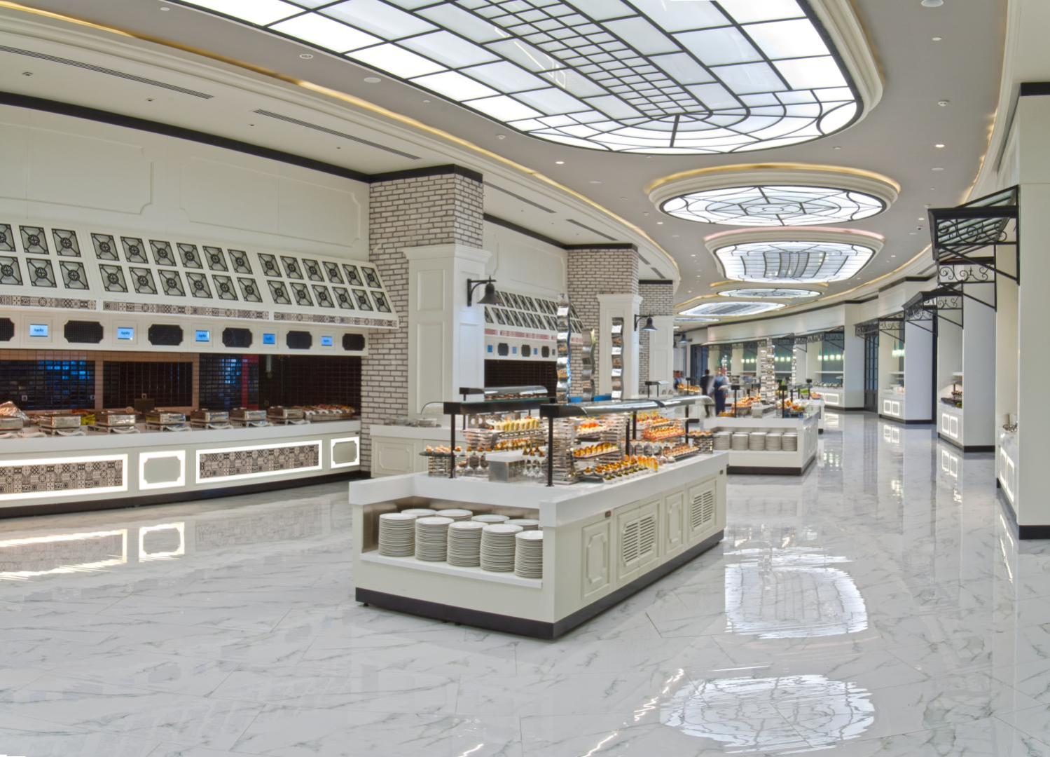 Sueno Hotels Deluxe Belek galvenais restorāns ar plašu bufetes zonu, marmora grīdām un modernu apgaismojumu Antalijas reģionā, Turcijā