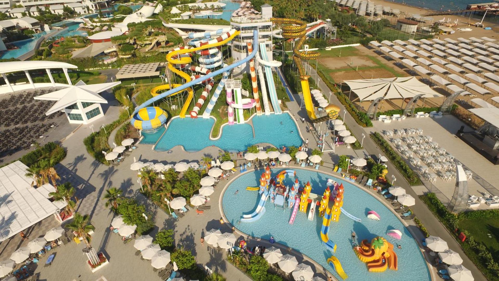 Sueno Hotels Deluxe Belek akvaparks ar krāsainiem slidkalniņiem pieaugušajiem un bērnu ūdens pilsētiņu seklajā baseinā