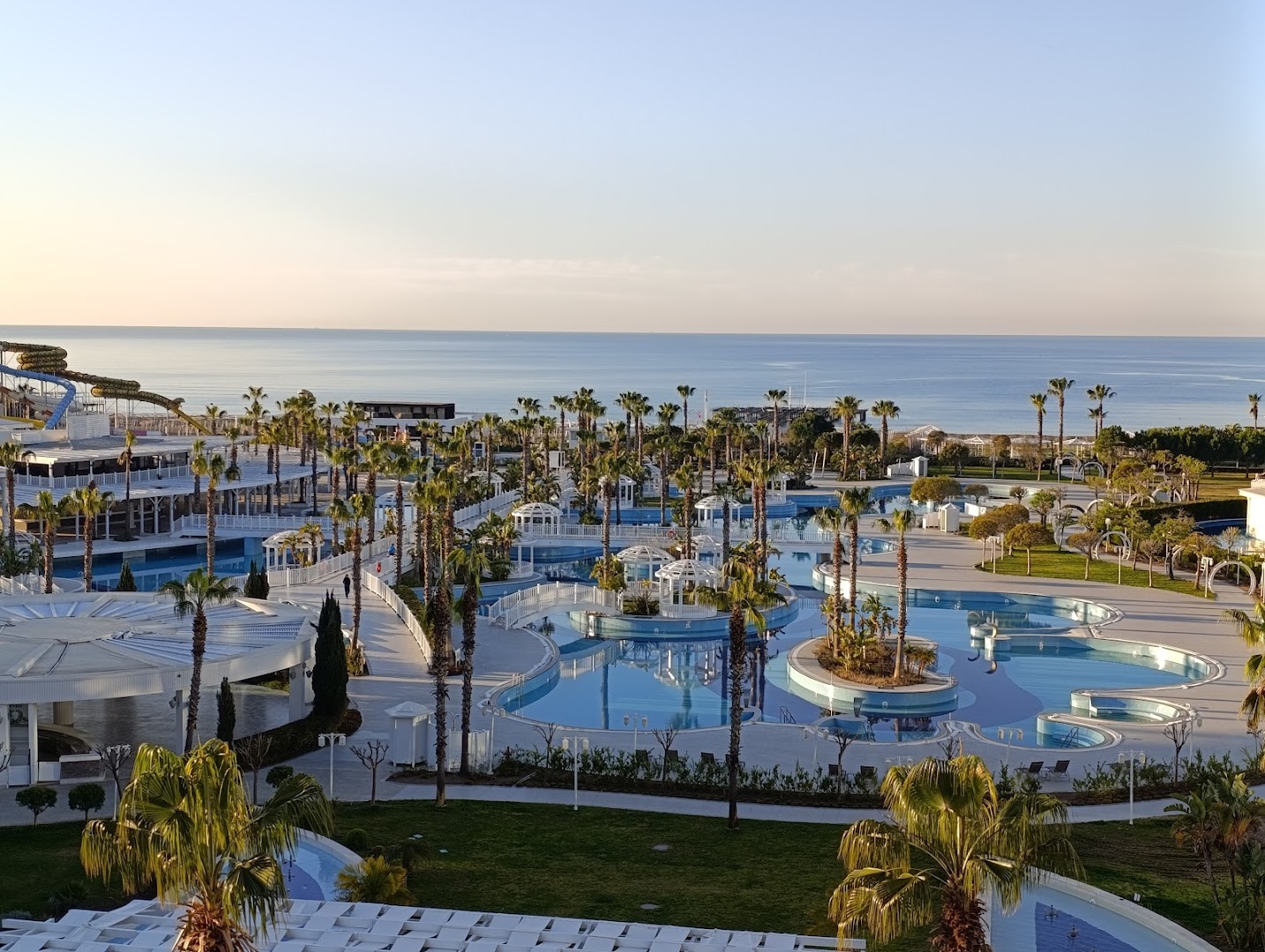 Sueno Hotels Golf Belek plašais āra baseinu komplekss ar palmām un skatu uz Vidusjūru Belekā, Turcijā — atpūtas zona un ūdens slidkalniņi