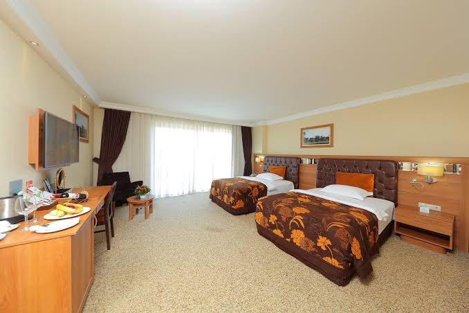 Sueno Hotels Golf Belek gaišs divvietīgs numurs ar divām gultām, rakstāmgaldu, televizoru un plašu logu Belekas kūrortā, Turcijā