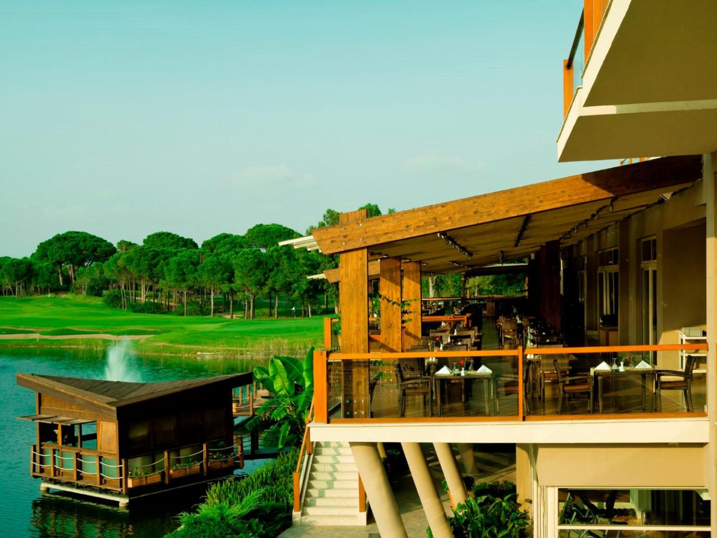 Sueno Hotels Golf Belek viesnīcas ēkas fasāde un terase pie ezera ar strūklaku un apkārtējo golfa laukumu ainavu Belekā