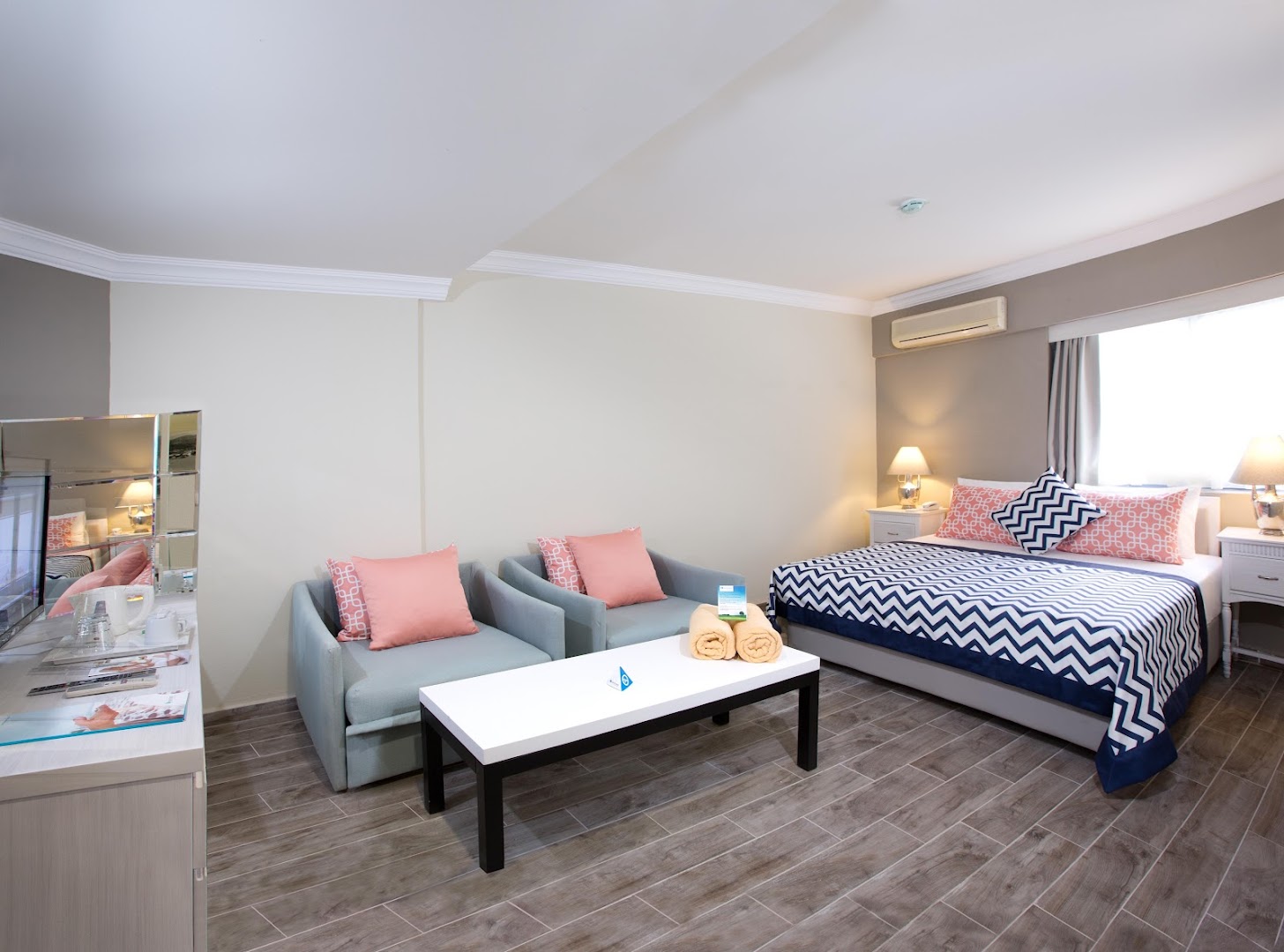 Paloma Marina Suites viesnīcas numurs ar divguļamo gultu, atpūtas krēsliem un gaišu interjeru Kušadasi reģionā Turcijā