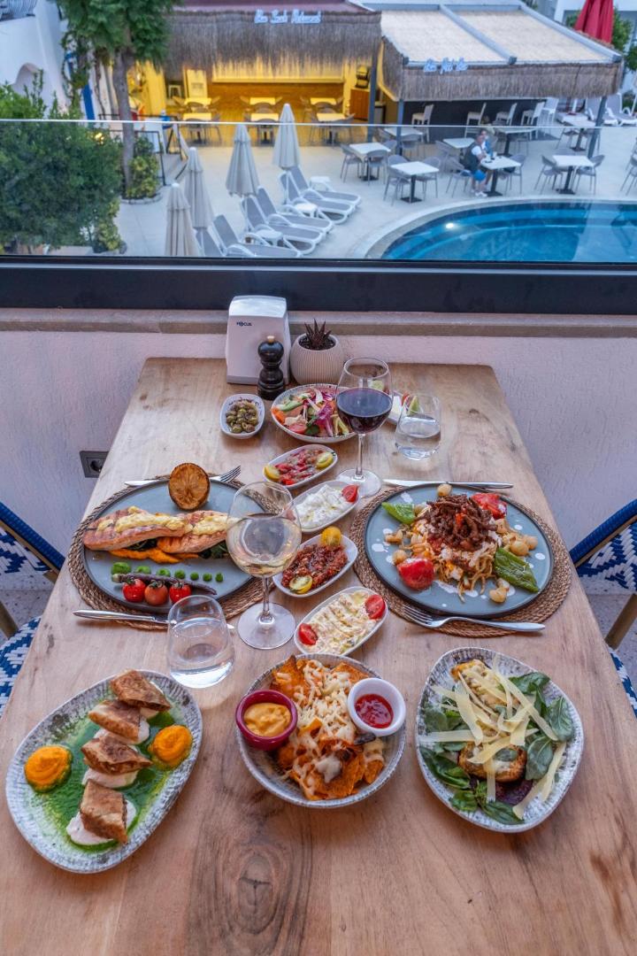 Tuvplāns ar bagātīgu ēdienu klāstu uz koka galda Paloma Marina Suites restorānā, tostarp zivju ēdieni un uzkodas