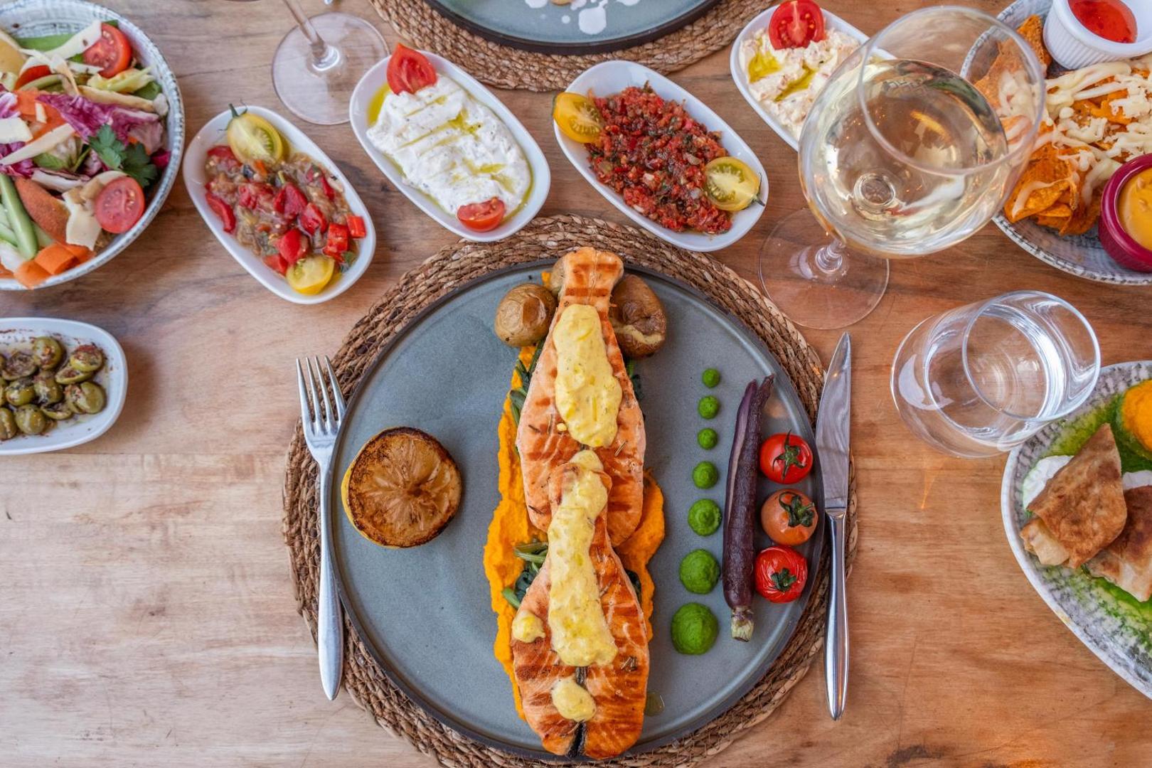 Paloma Marina Suites restorāna servējums ar grilētu lasi, dārzeņu biezeni un tradicionālām meze uzkodām — skats no augšas uz koka galda