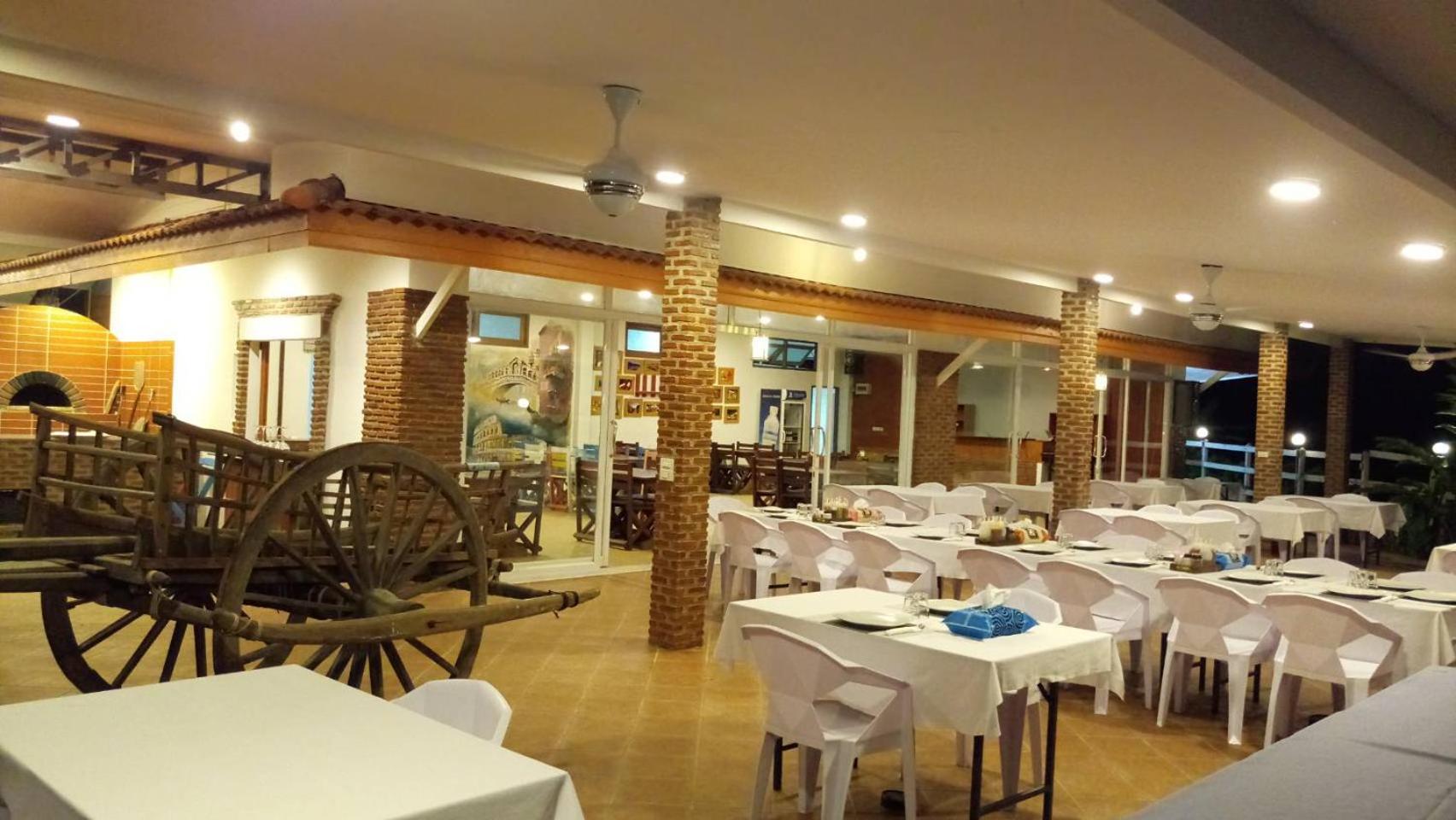 Armonia Holiday Village & Spa restorāna interjers ar dekoratīviem koka ratiem, balti klātiem galdiem un ķieģeļu kolonnām