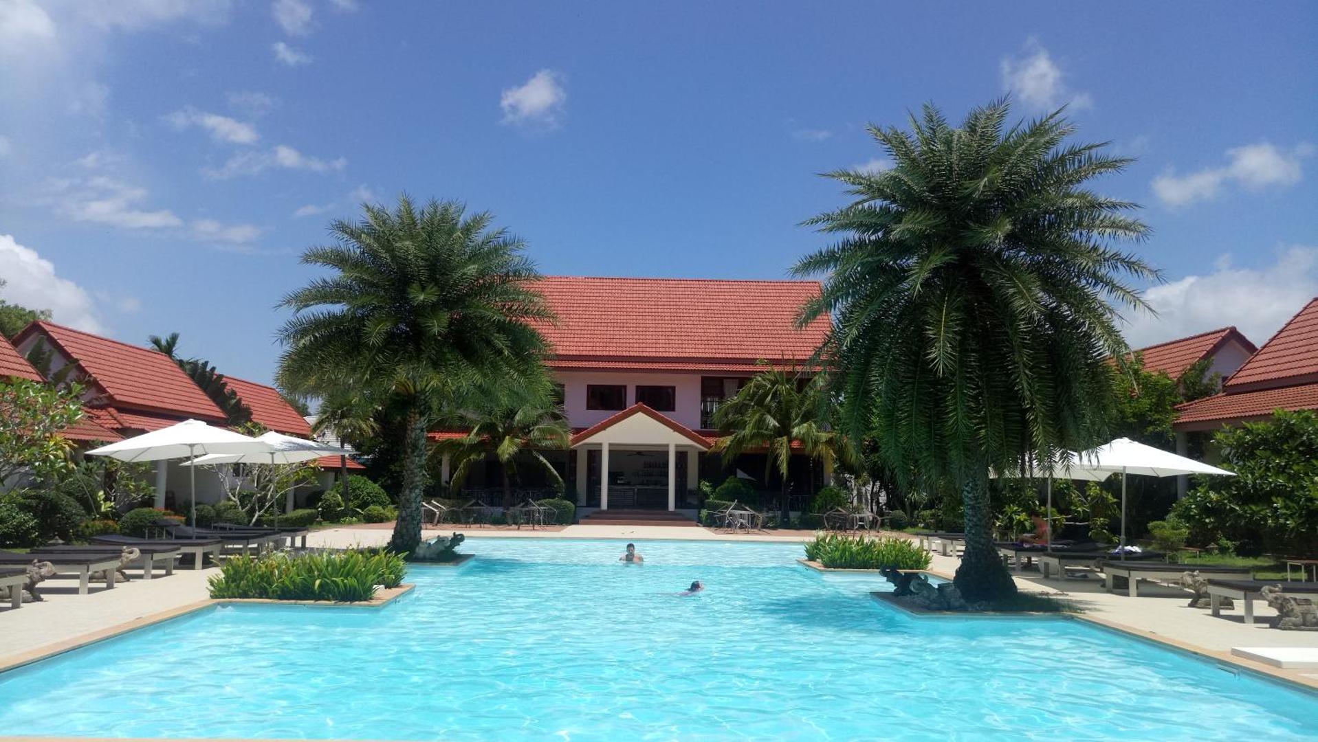 Viesnīcas Armonia Holiday Village & Spa teritorija ar baseinu, palmām un tradicionāla stila ēkām ar sarkaniem jumtiem.