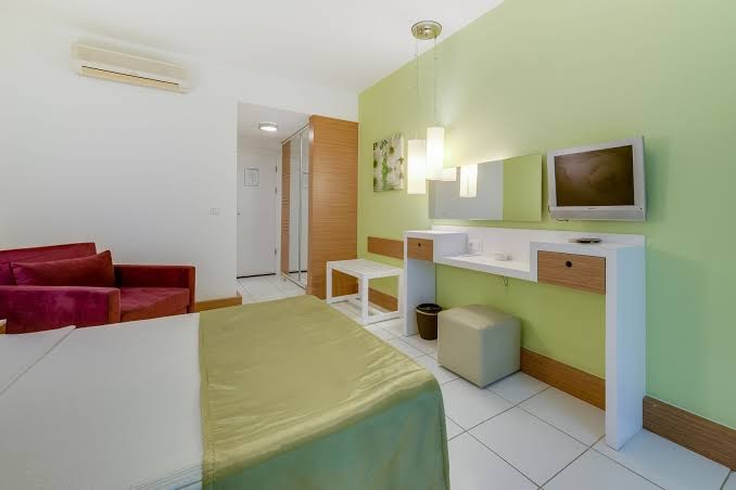 Mūsdienīgs Armonia Holiday Village & Spa viesnīcas numurs ar zaļu akcenta sienu, darba zonu un ērtu atpūtas krēslu
