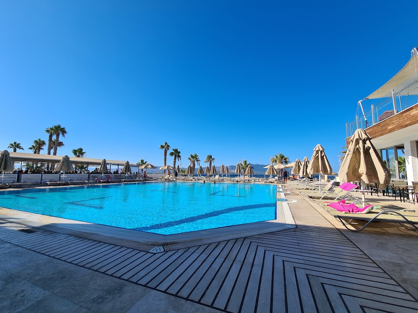 Armonia Holiday Village & Spa galvenais āra baseins ar saulessargiem un atpūtas krēsliem Bodrumas piekrastē, Turcijā saulainā dienā.