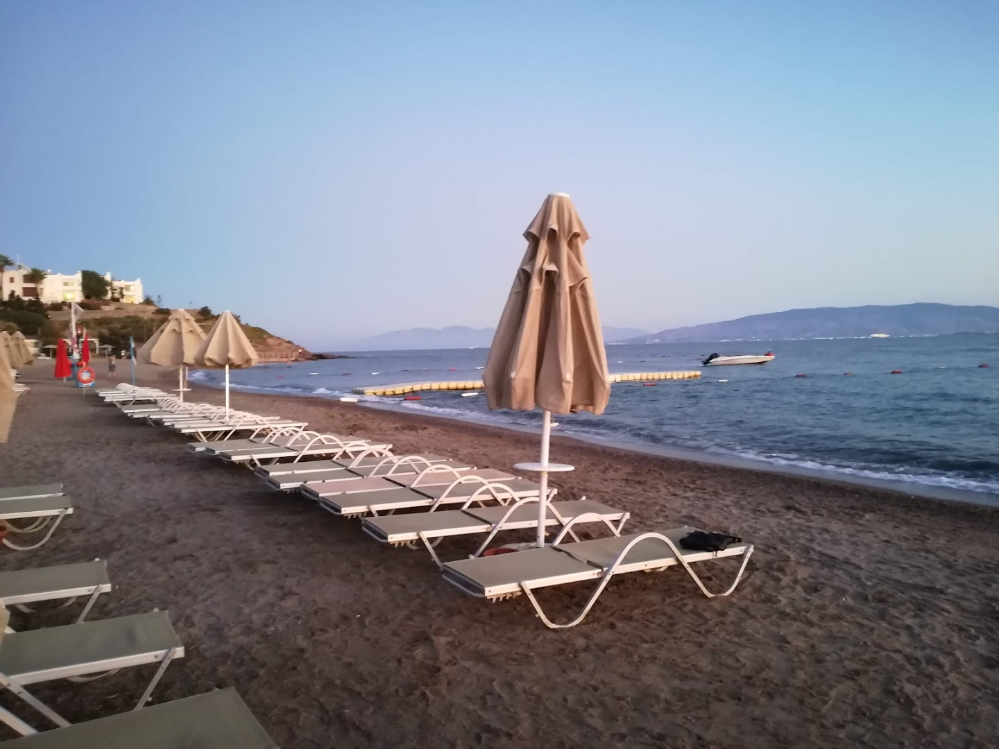 Viesnīcas Armonia Holiday Village & Spa privātā pludmale ar sauļošanās krēsliem un skatu uz kalniem tālumā