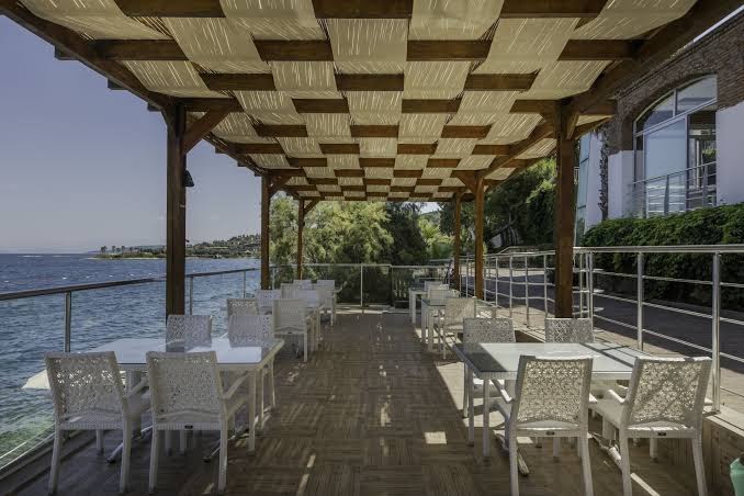 Blue Dreams Resort & Spa restorāna terase tieši pie ūdens ar baltiem galdiem un dekoratīvu koka nojumi