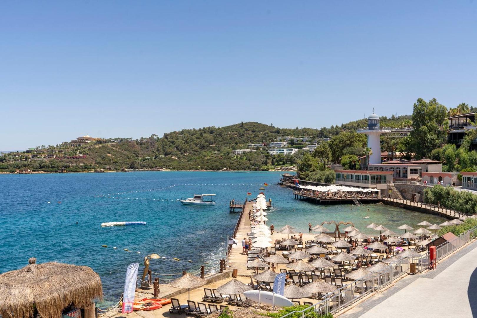 Blue Dreams Resort privātā pludmale ar saulessargiem un koka piestātni Bodrumas piekrastē — dzidrs ūdens un kalnains fons