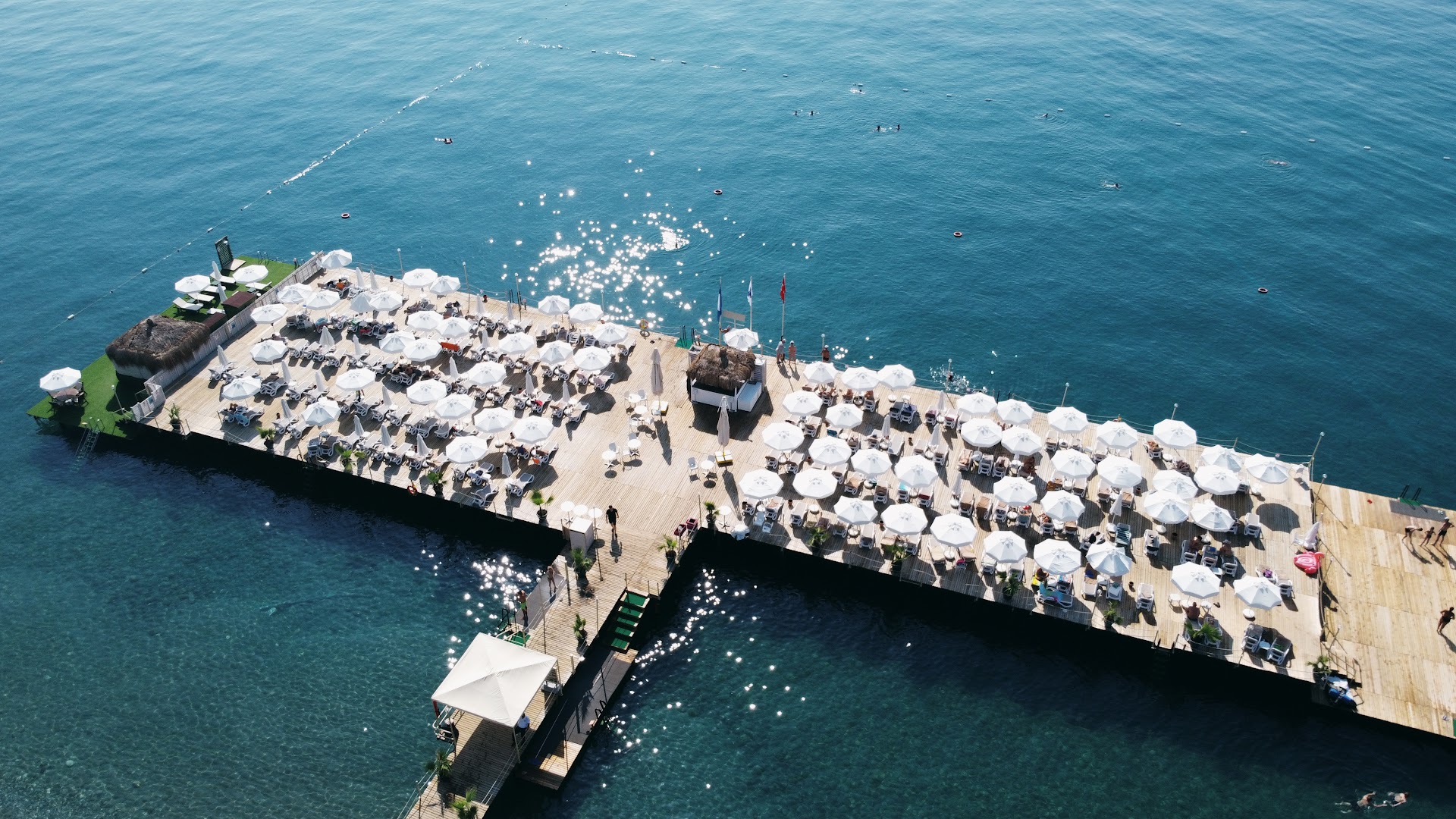 Ulusoy Kemer Holiday Club mola atpūtas zona ar baltiem saulessargiem un kāpnēm uz jūru saulainā dienā