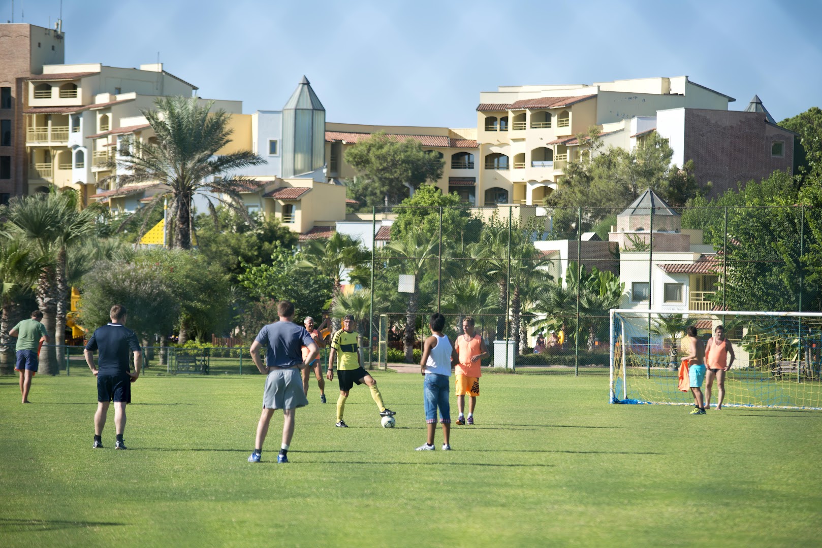 Limak Arcadia Sport Resort futbola laukums ar spēlētājiem un viesnīcas ēkām fonā Belekā — sporta aktivitātes zaļā teritorijā