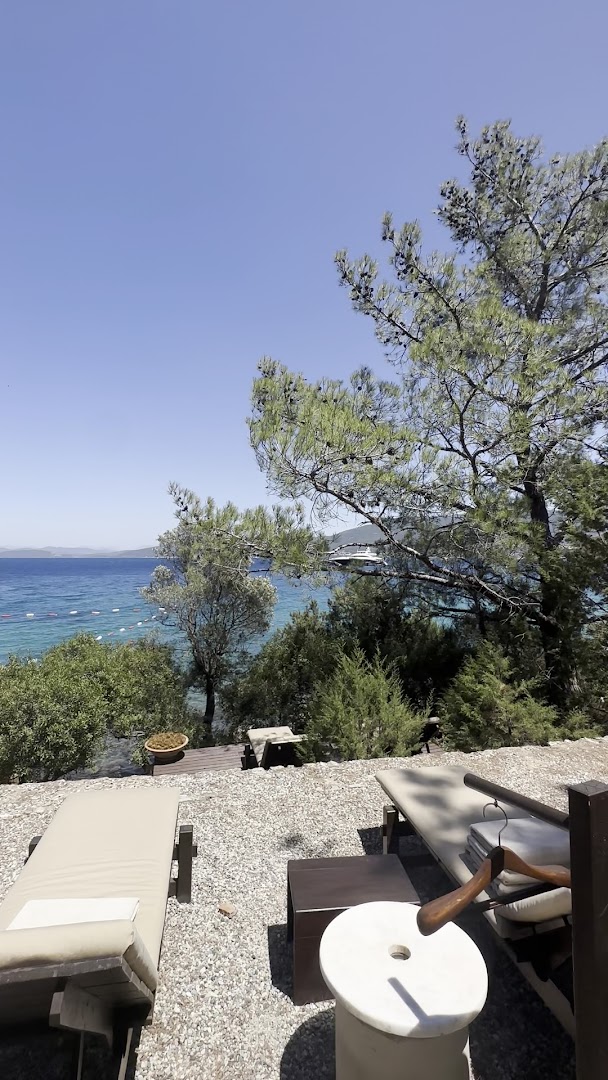 Amanruya Resort sauļošanās krēsli priežu meža ēnā ar skatu uz zilo Egejas jūru un jahtu tālumā Bodrumā