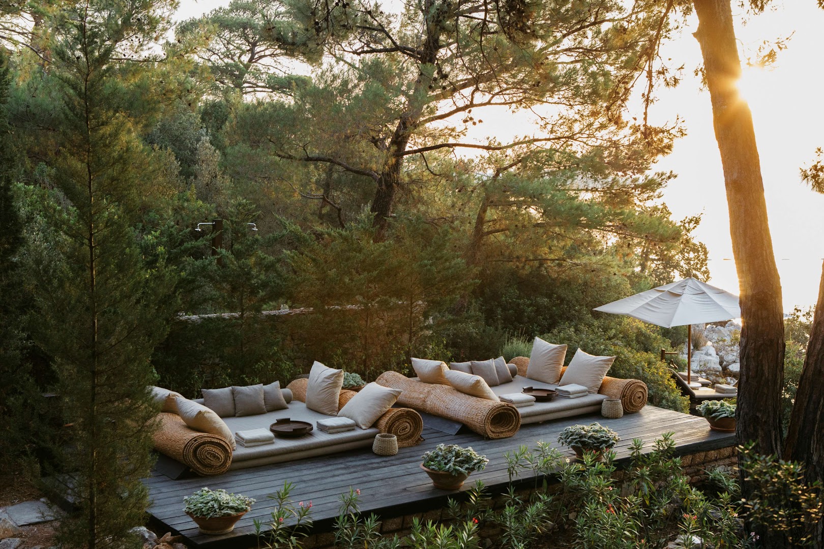 Amanruya Resort āra atpūtas zona priežu meža piekrastē ar mīkstiem zviļņiem uz koka terases saulrieta gaismā