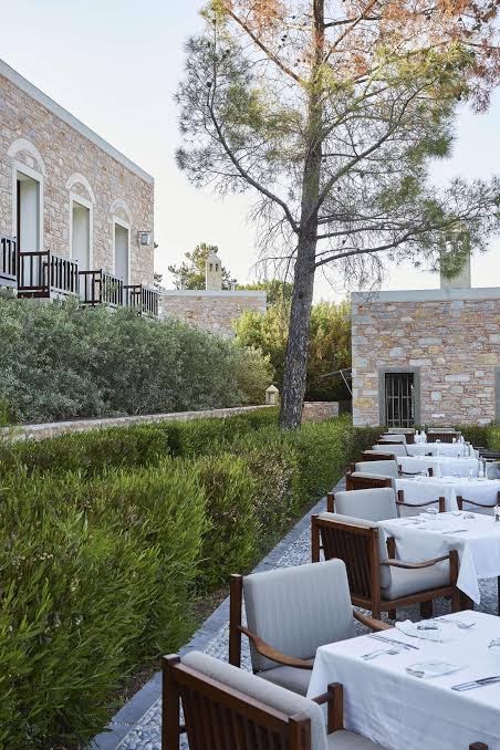 Amanruya Resort Hotel āra terases restorāns Bodrumā ar balti klātiem galdiem, koka krēsliem un skatu uz akmens mūra ēkām un dārzu.