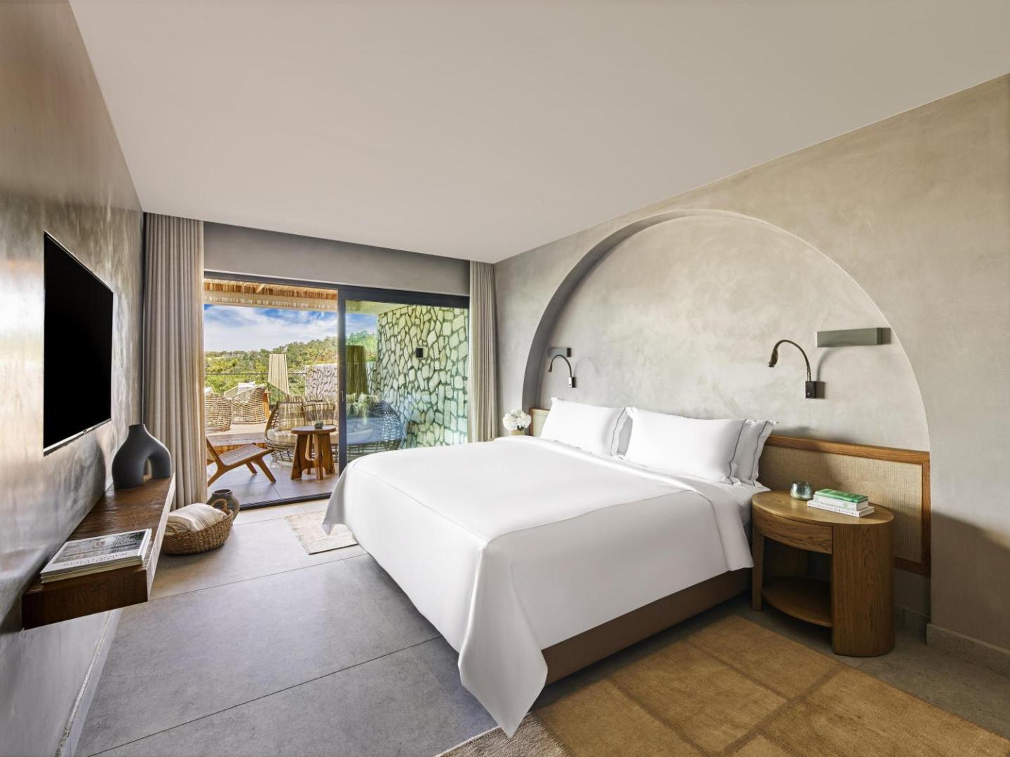 Rixos Premium Bodrum numurs ar lielu gultu, sienas nišu un izeju uz balkonu ar skatu uz dārzu