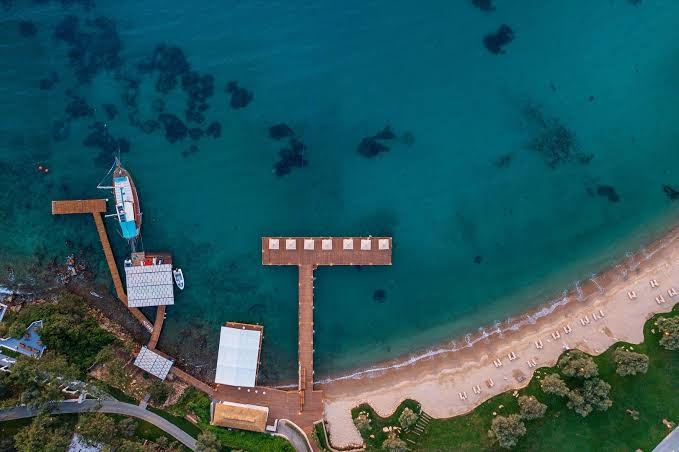 Rixos Premium Bodrum koka piestātne un laipas virs dzidrā Egejas jūras ūdens — skats no augšas uz atpūtas zonu