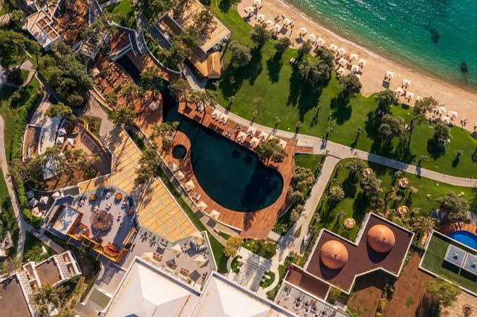 Rixos Premium Bodrum teritorijas skats no augšas uz baseinu, dārzu, gājēju celiņiem un pludmales zonu ar saulessargiem