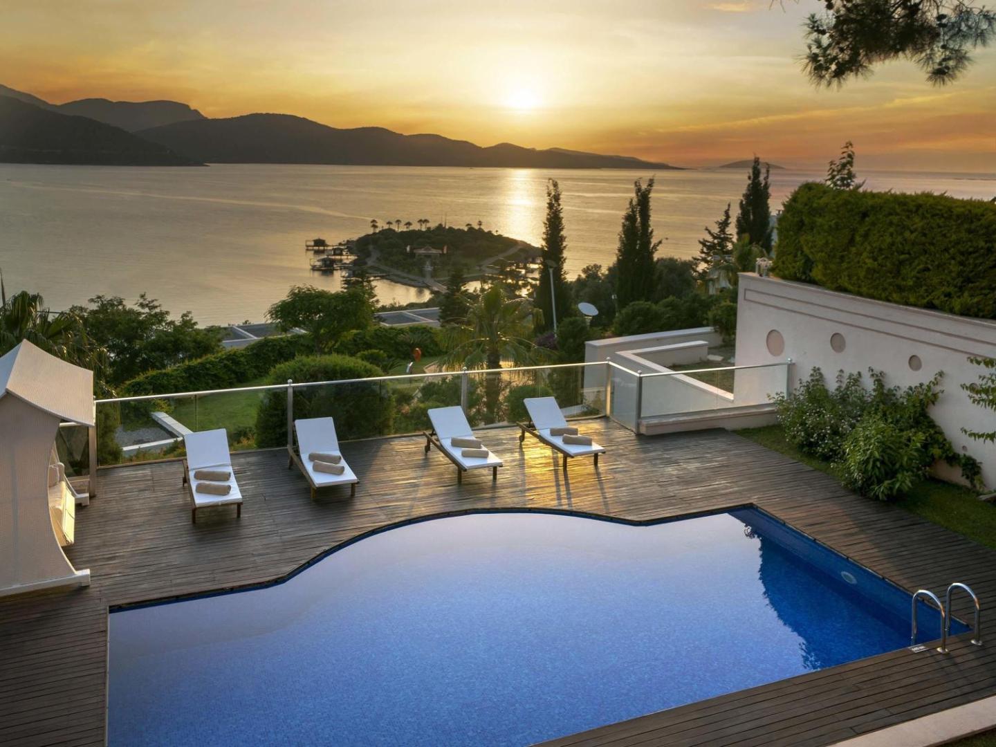 Rixos Premium Bodrum villas terase ar baseinu saulrietā, skatu uz pussalu un Egejas jūru zelta stundā