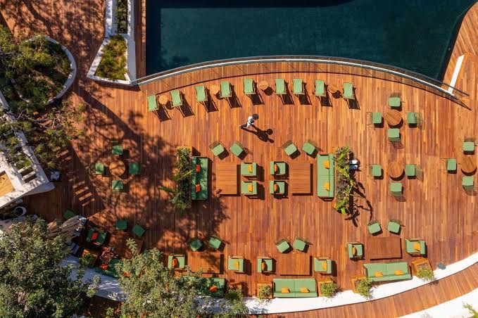 Rixos Premium Bodrum āra atpūtas zona no putna lidojuma ar koka terasi, dīvāniem un baseina malu