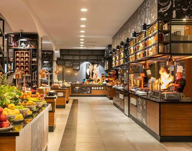 Rixos Premium Bodrum bufetes tipa restorāna interjers ar plašu augļu izvēli un atvērto virtuvi
