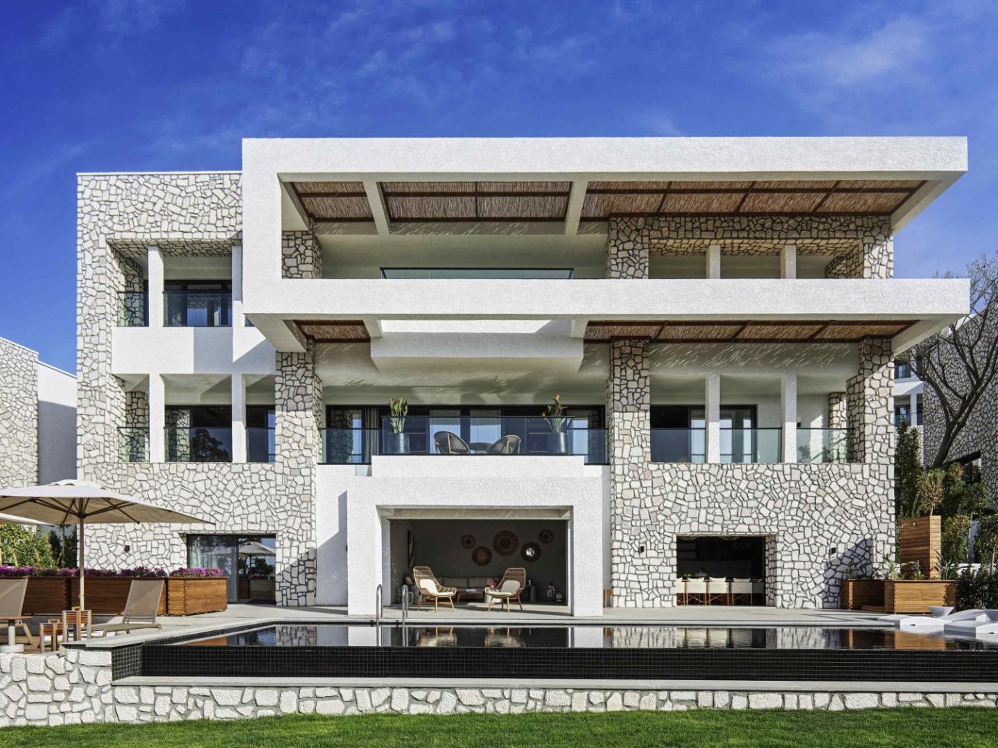 Rixos Premium Bodrum modernas arhitektūras villa ar akmens apdari, privātu baseinu un plašām terasēm saulainā dienā