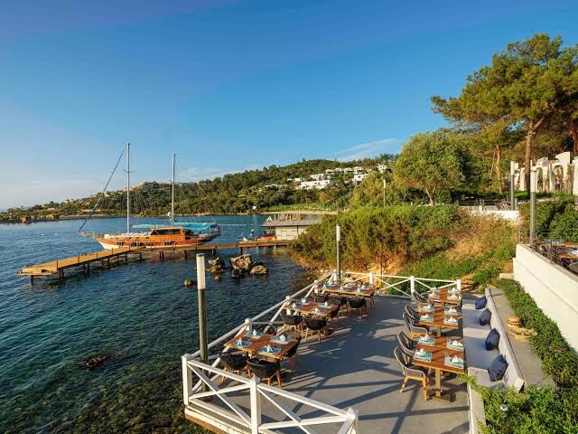 Rixos Premium Bodrum restorāna terase pie jūras ar skatu uz piestātni un jahtām piekrastē saulainā dienā