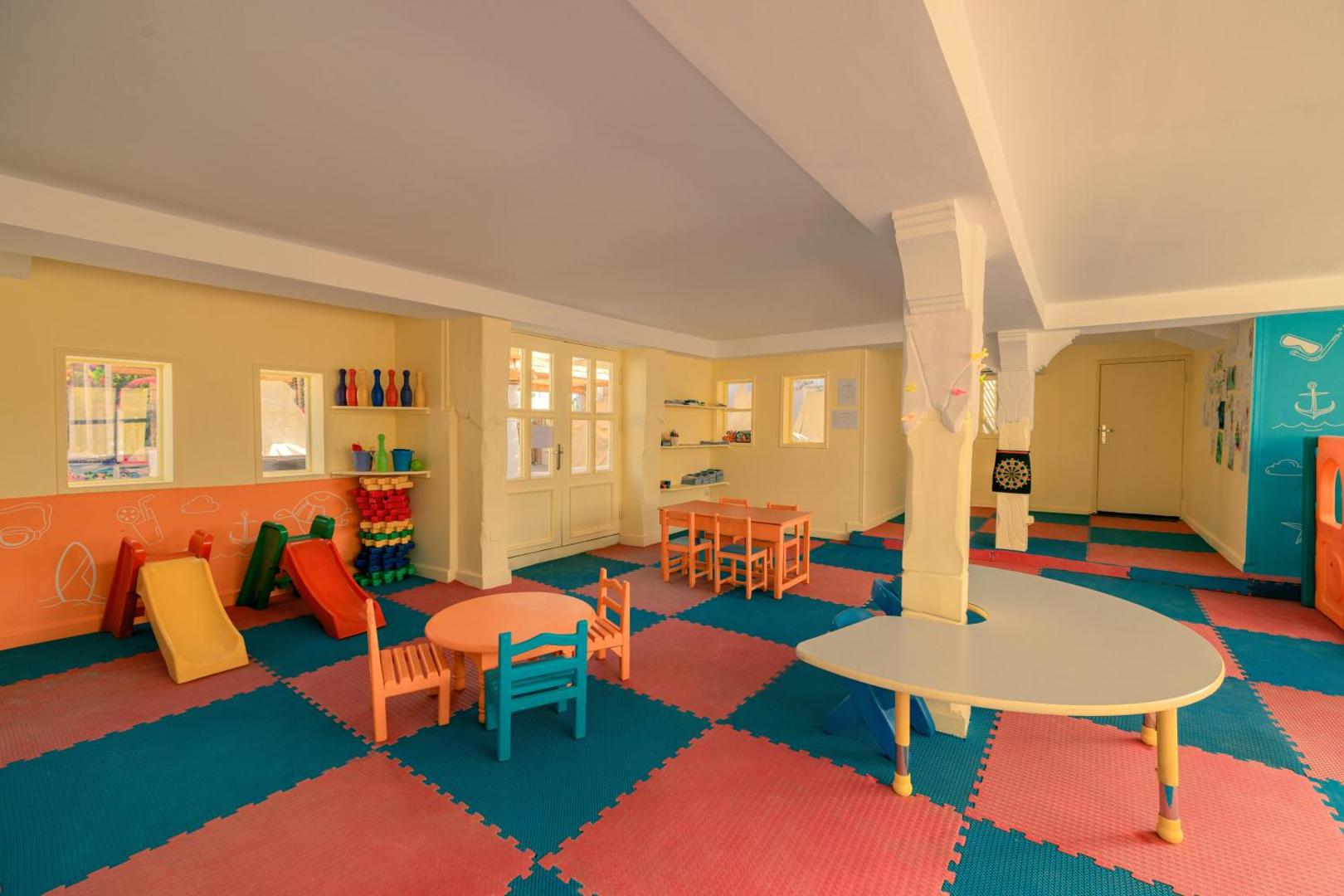 Jaz Sharm Dreams Resort bērnu kluba iekštelpas ar krāsainu mīksto grīdu, maziem galdiņiem un rotaļu slidkalniņiem drošai izklaidei