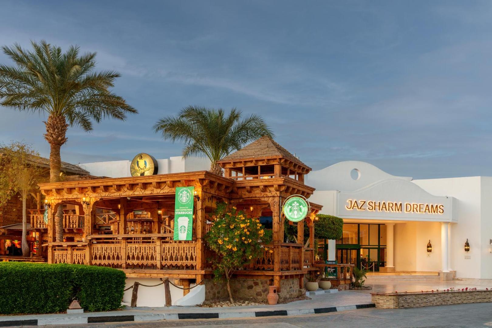 Jaz Sharm Dreams Resort teritorijā esošā koka konstrukcijas kafejnīca ar Starbucks zīmi, ko ieskauj palmas un ziedoši krūmi