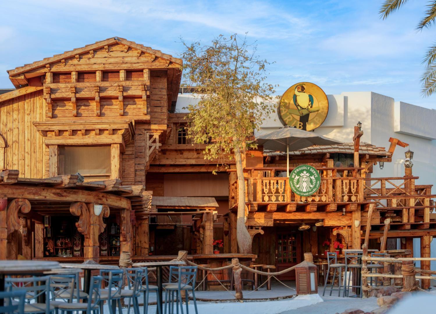 Jaz Sharm Dreams Resort koka arhitektūras bārs un kafejnīca Šarm eš Šeihā — mājīga āra terase ar galdiņiem un Starbucks kafijas stendu