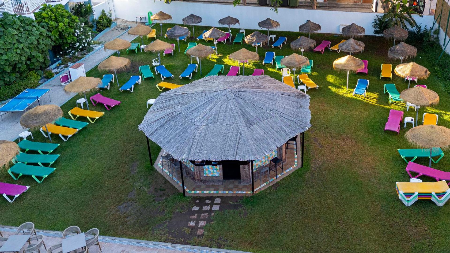 MedPlaya Hotel Alba Beach dārza bārs ar salmu jumtu, ko ieskauj krāsaini zviļņi un saulessargi zaļā zālienā