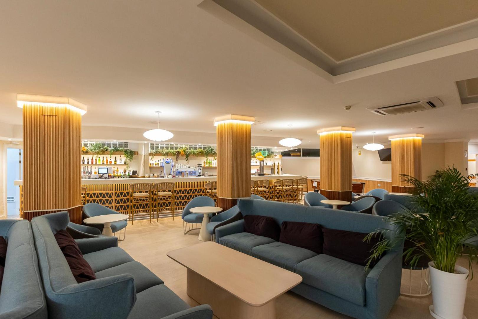 Mūsdienīgs MedPlaya Hotel Alba Beach lobby bārs ar ziliem dīvāniem, koka apdares kolonnām un siltu apgaismojumu vakara atpūtai